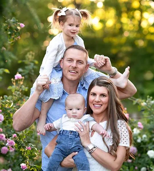 Greg Harris with his daughter on his shoulders, his wife, and their baby son in a garden